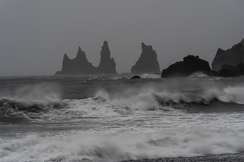 Fine art landscape photograph of the jagged Reynisdrangar basalt sea stacks at Reynisfjara black sand beach in Iceland during a dramatic torrential rain storm, featured on timeprints.com.